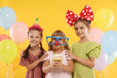 Photo of Birthday celebration. Kids with cupcake and balloons on orange background