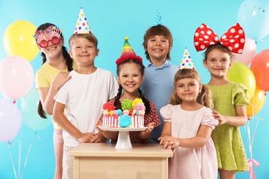 Photo of Birthday celebration. Happy kids with tasty cake and festive decor on light blue background