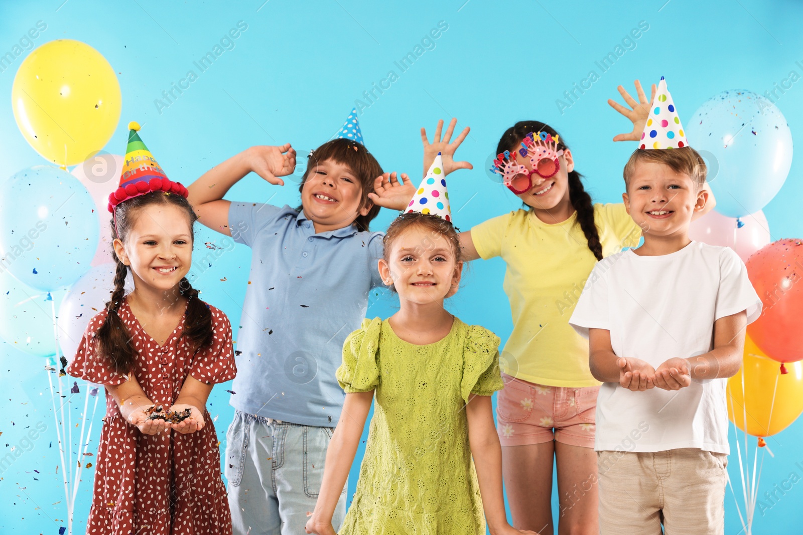 Birthday celebration. Happy kids with festive decor on light blue background Photo of Birthday celebration. Happy kids with festive decor on light blue background