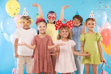 Photo of Birthday celebration. Happy kids with festive decor under falling confetti on light blue background