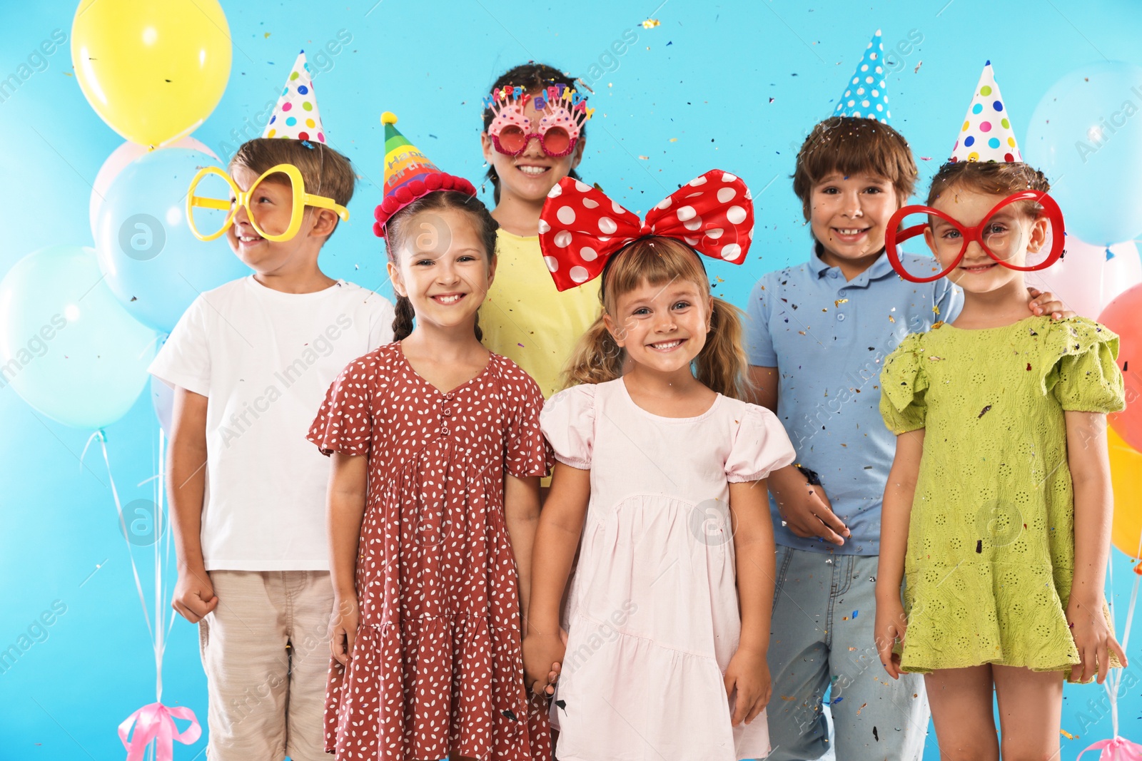 Birthday celebration. Happy kids with festive decor under falling confetti on light blue background Photo of Birthday celebration. Happy kids with festive decor under falling confetti on light blue background