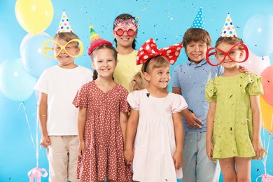 Photo of Birthday celebration. Happy kids with festive decor under falling confetti on light blue background