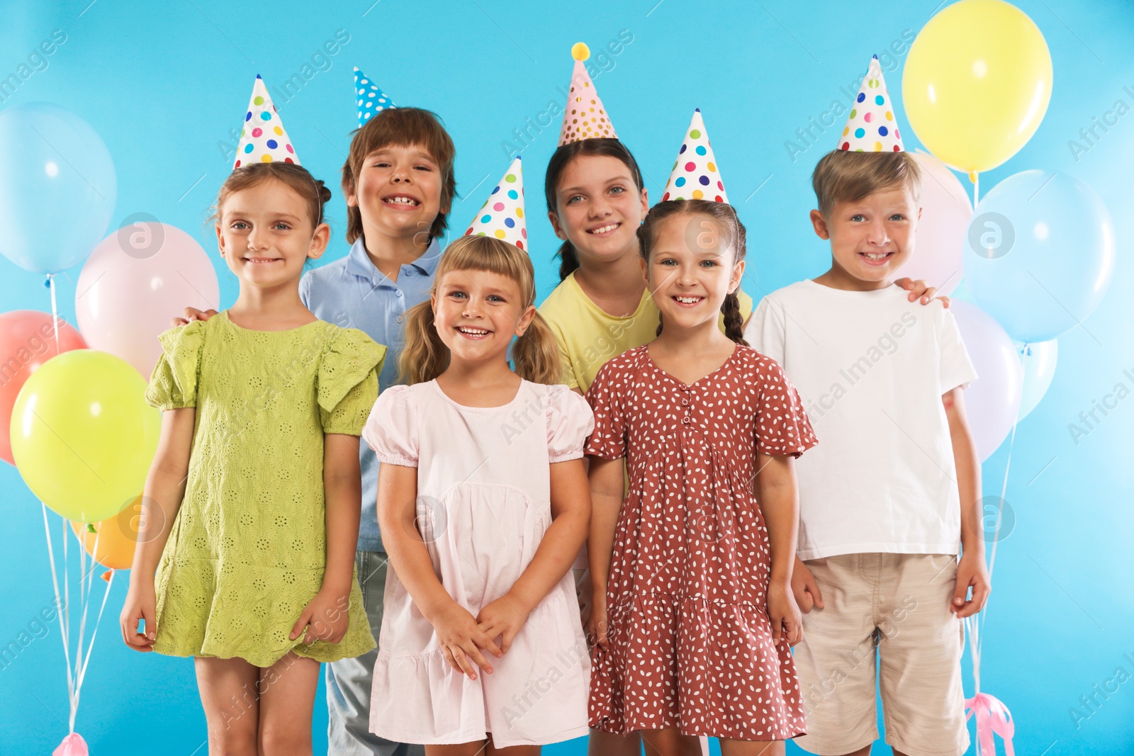 Birthday celebration. Happy kids in party hats and balloons on light blue background Photo of Birthday celebration. Happy kids in party hats and balloons on light blue background