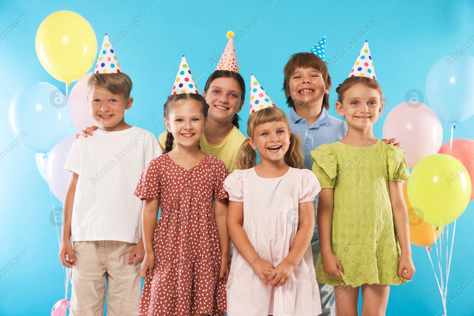 Birthday celebration. Happy kids in party hats and balloons on light blue background Photo of Birthday celebration. Happy kids in party hats and balloons on light blue background