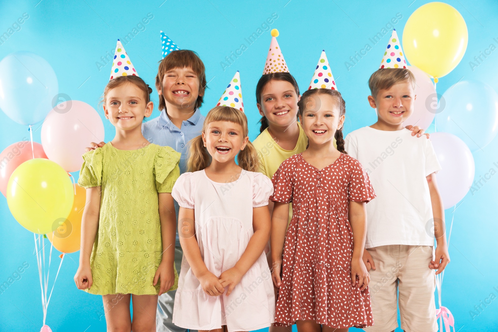 Birthday celebration. Happy kids in party hats and balloons on light blue background Photo of Birthday celebration. Happy kids in party hats and balloons on light blue background