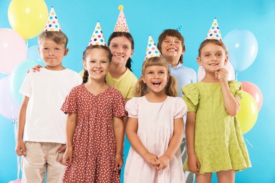 Photo of Birthday celebration. Happy kids in party hats and balloons on light blue background