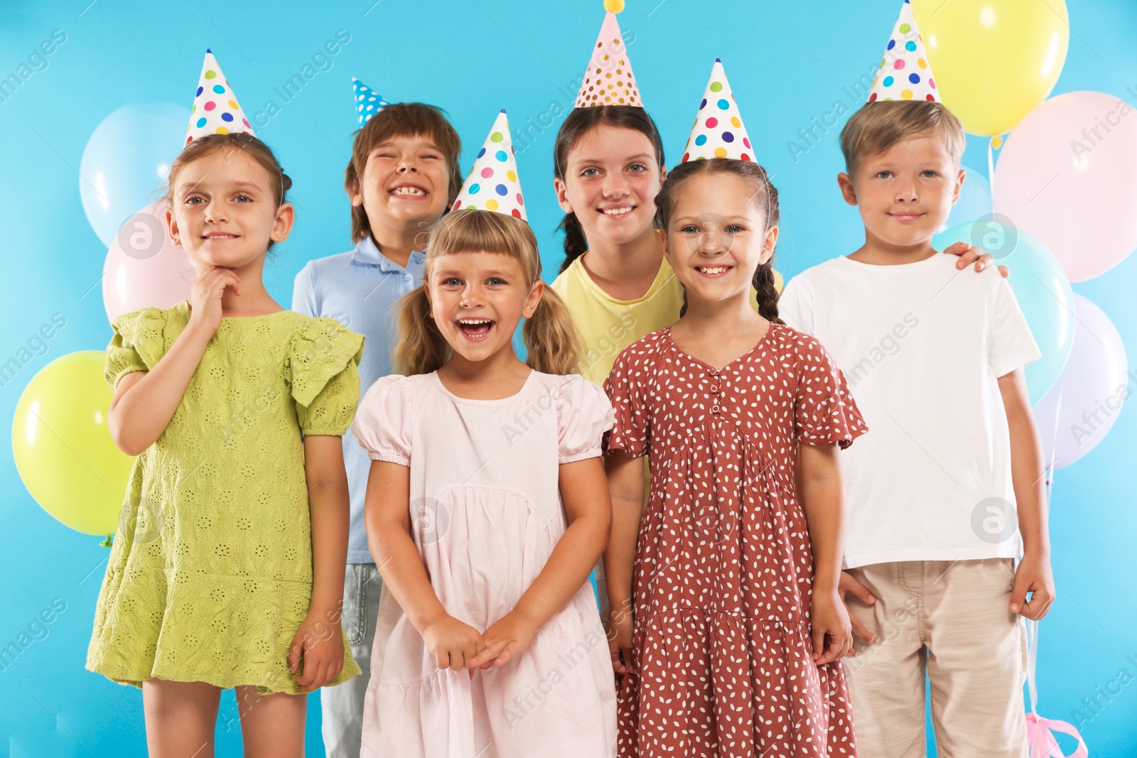 Birthday celebration. Happy kids in party hats and balloons on light blue background Photo of Birthday celebration. Happy kids in party hats and balloons on light blue background