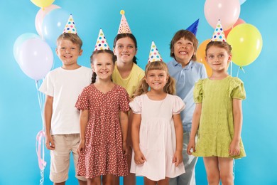 Photo of Birthday celebration. Happy kids in party hats and balloons on light blue background