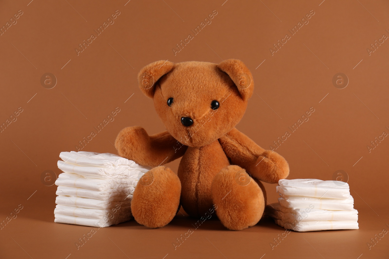 Toy bear and diapers on brown background. Baby accessories Photo of Toy bear and diapers on brown background. Baby accessories