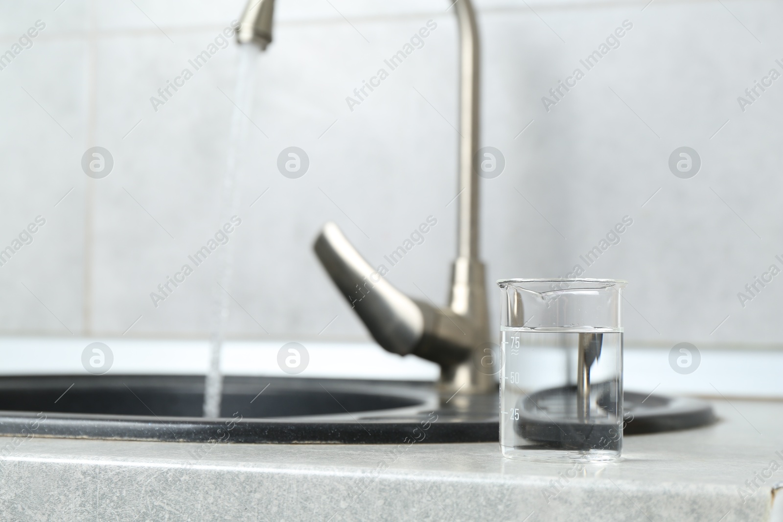 Photo of Beaker with clean water near sink on counter in kitchen, closeup. Space for text