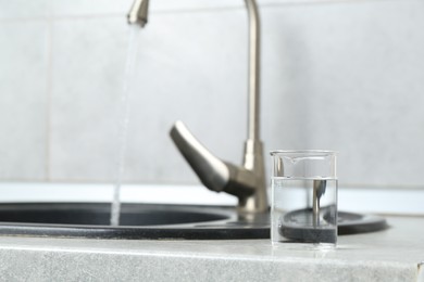 Photo of Beaker with clean water near sink on counter in kitchen, closeup. Space for text