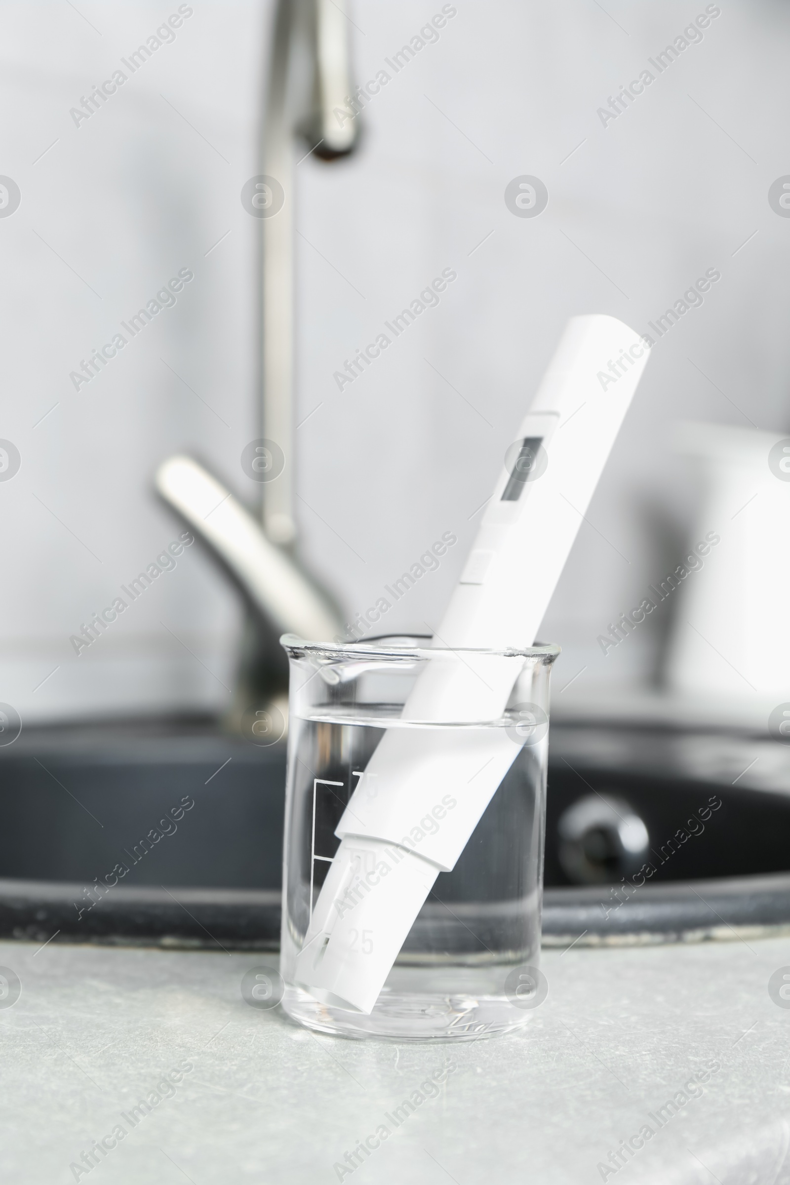 Beaker with clean water and digital pH meter near sink on counter in kitchen, closeup Photo of Beaker with clean water and digital pH meter near sink on counter in kitchen, closeup