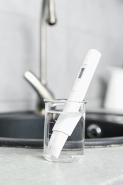 Photo of Beaker with clean water and digital pH meter near sink on counter in kitchen, closeup