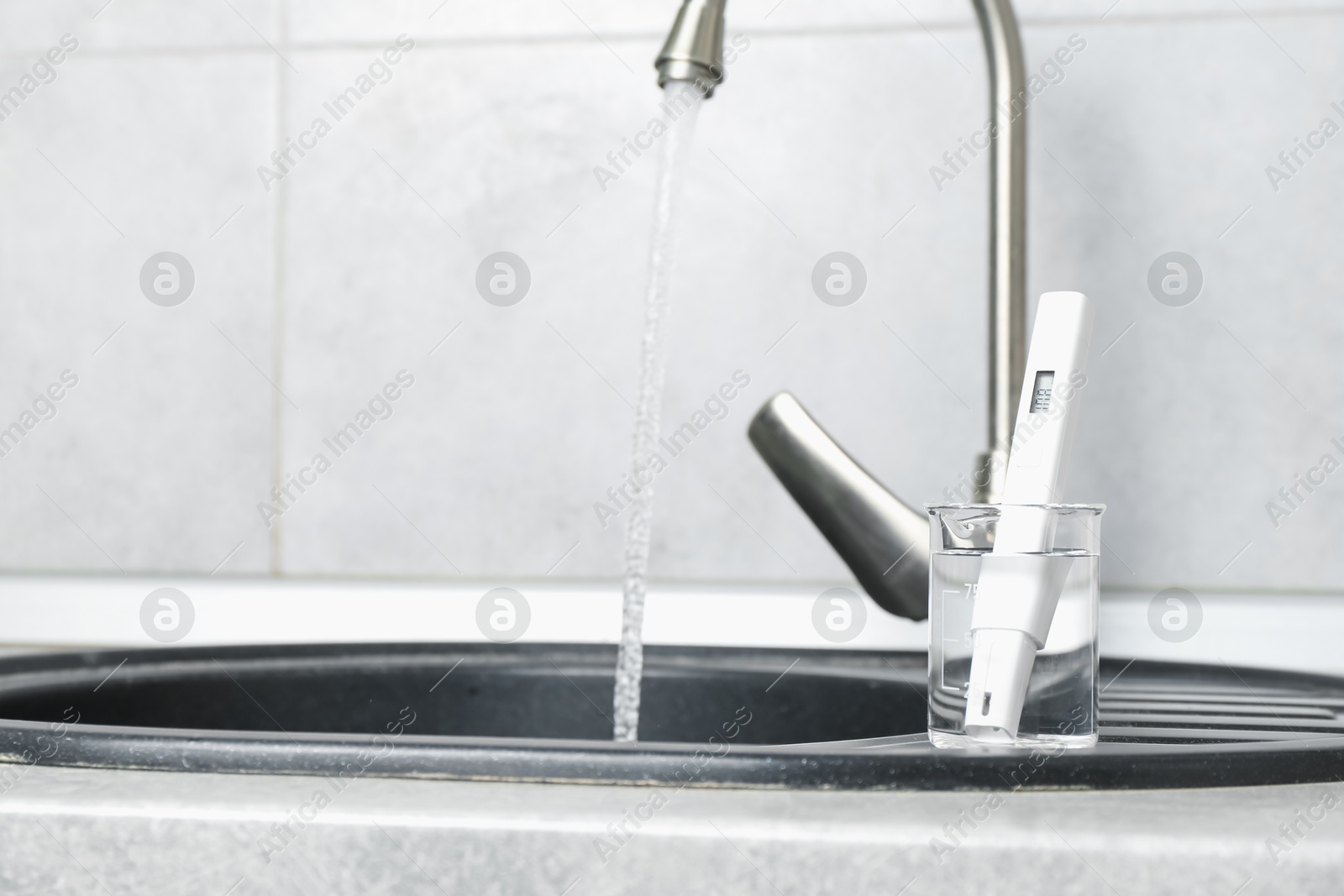 Beaker with clean water and digital pH meter near sink on counter in kitchen, closeup. Space for text Photo of Beaker with clean water and digital pH meter near sink on counter in kitchen, closeup. Space for text
