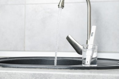 Photo of Beaker with clean water and digital pH meter near sink on counter in kitchen, closeup. Space for text