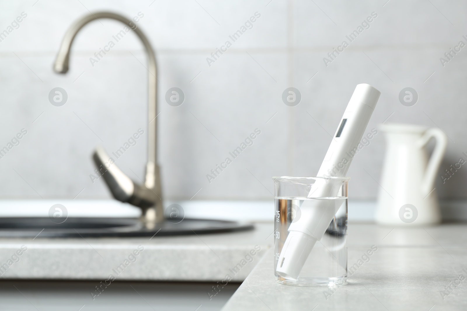 Beaker with clean water and digital pH meter near sink on counter in kitchen, closeup. Space for text Photo of Beaker with clean water and digital pH meter near sink on counter in kitchen, closeup. Space for text