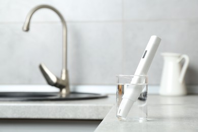 Photo of Beaker with clean water and digital pH meter near sink on counter in kitchen, closeup. Space for text