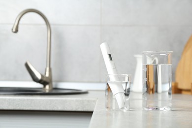 Photo of Beakers with clean water and digital pH meter near sink on counter in kitchen, closeup. Space for text