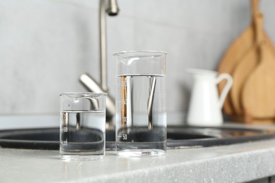 Photo of Beakers with clean water near sink on counter in kitchen, closeup