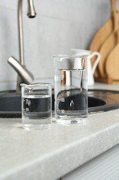 Photo of Beakers with clean water near sink on counter in kitchen, closeup
