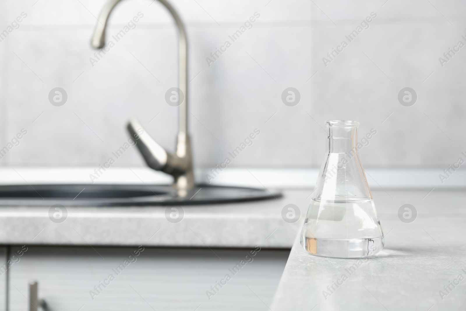 Flask with clean water near sink on counter in kitchen, closeup. Space for text Photo of Flask with clean water near sink on counter in kitchen, closeup. Space for text
