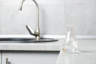 Photo of Flask with clean water near sink on counter in kitchen, closeup. Space for text