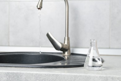 Photo of Flask with clean water near sink on counter in kitchen, closeup. Space for text