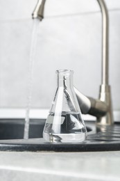 Photo of Flask with clean water near sink on counter in kitchen, closeup