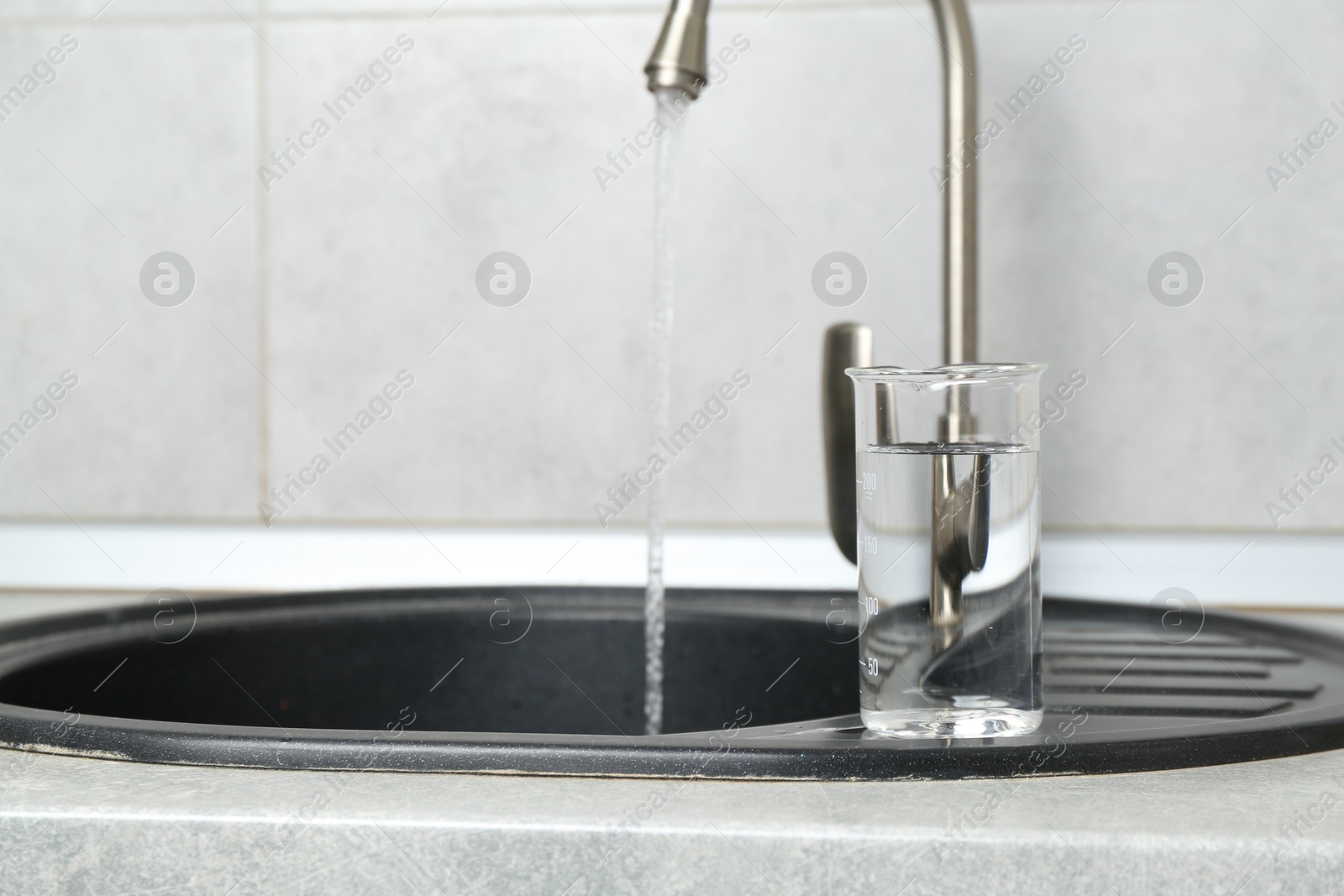 Beaker with clean water near sink on counter in kitchen, closeup. Space for text Photo of Beaker with clean water near sink on counter in kitchen, closeup. Space for text