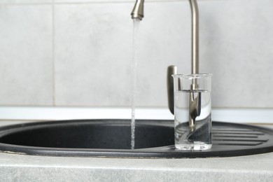 Photo of Beaker with clean water near sink on counter in kitchen, closeup. Space for text