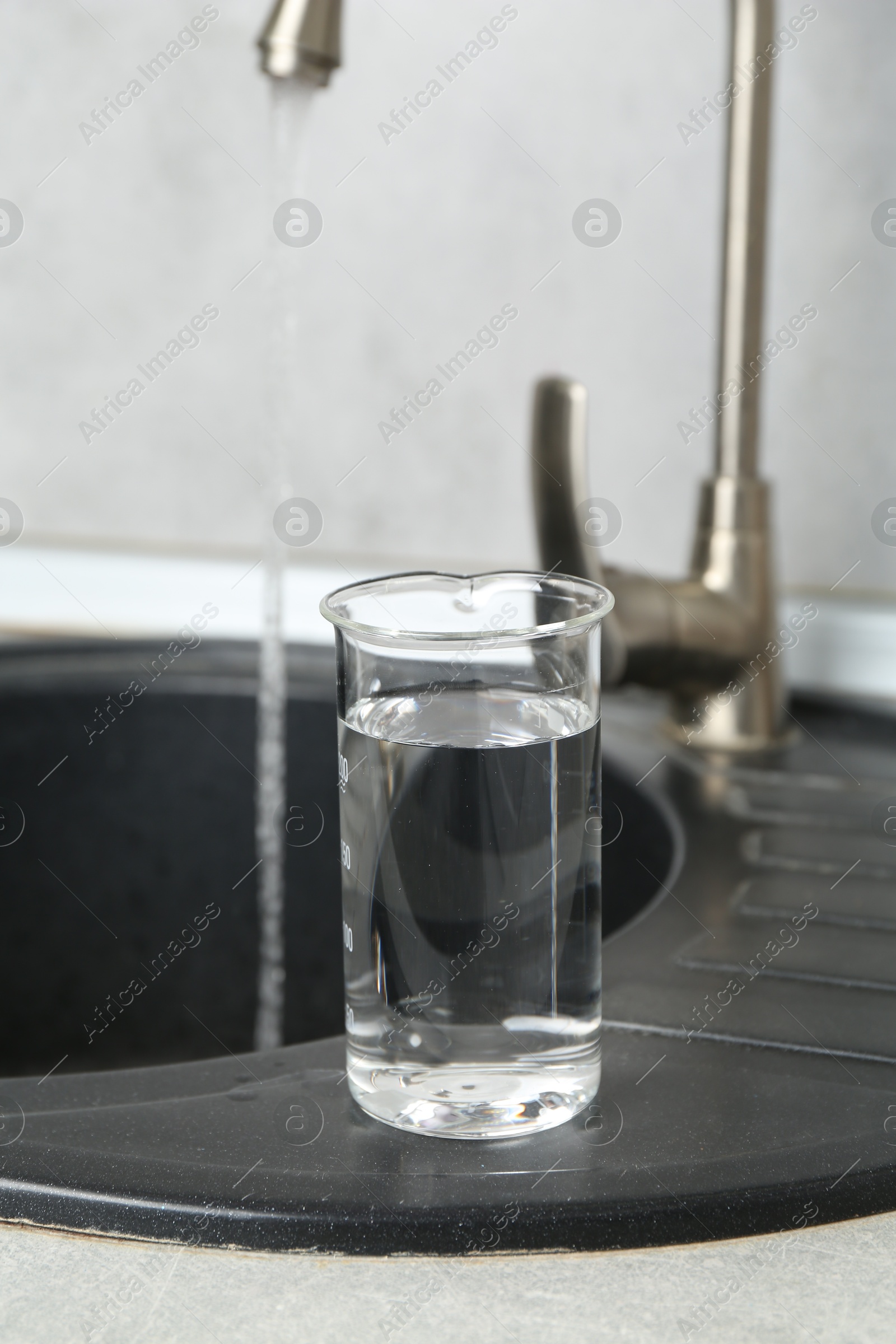 Beaker with clean water near sink on counter in kitchen, closeup Photo of Beaker with clean water near sink on counter in kitchen, closeup