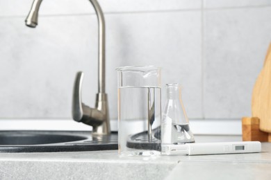Photo of Glassware with clean water and digital pH meter near sink on counter in kitchen, closeup