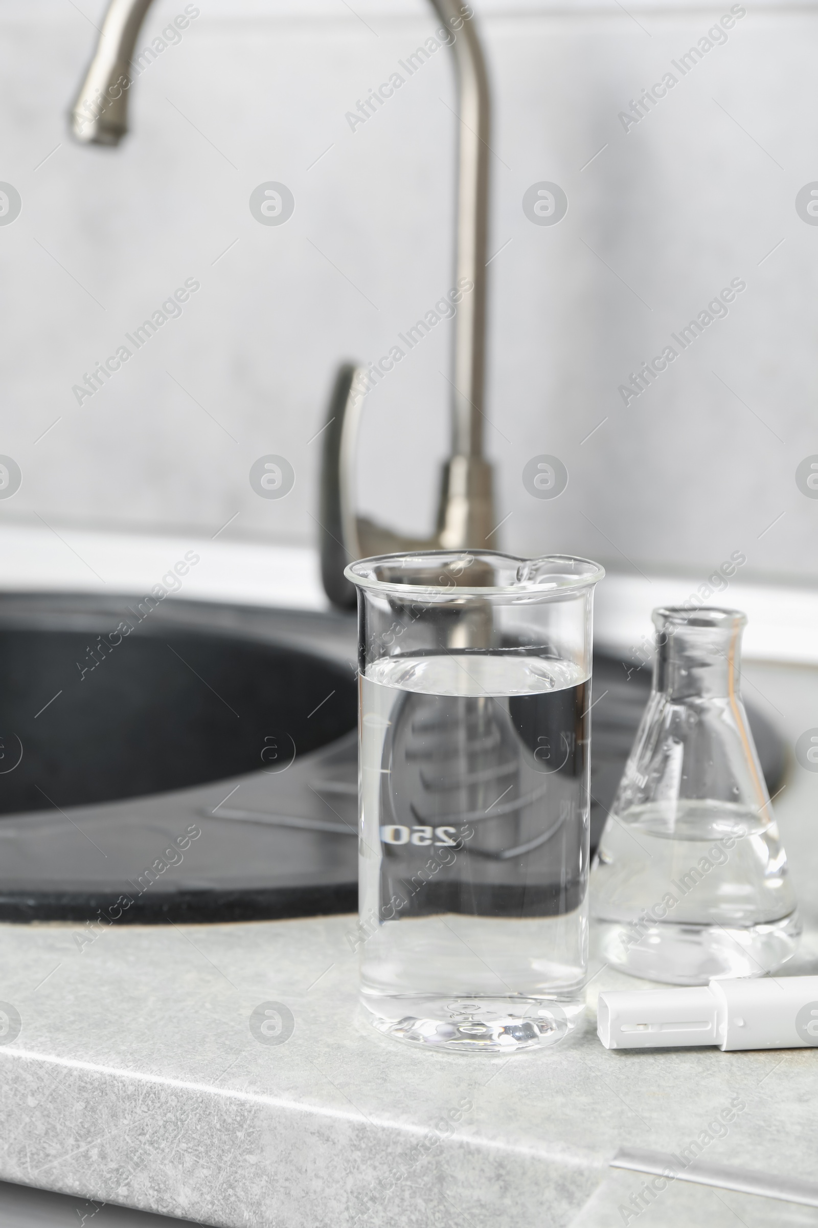 Glassware with clean water and digital pH meter near sink on counter in kitchen, closeup Photo of Glassware with clean water and digital pH meter near sink on counter in kitchen, closeup