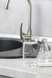 Photo of Glassware with clean water and digital pH meter near sink on counter in kitchen, closeup