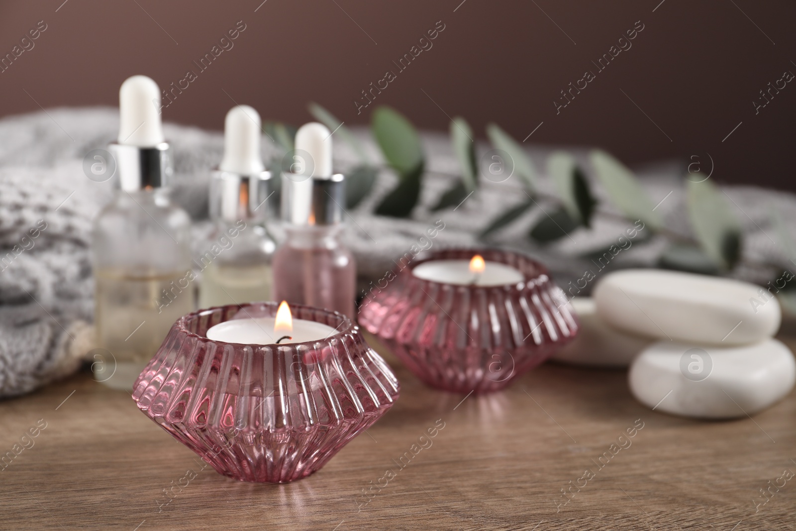 Composition with burning candles, spa stones and cosmetic products on wooden table against brown background, closeup Photo of Composition with burning candles, spa stones and cosmetic products on wooden table against brown background, closeup