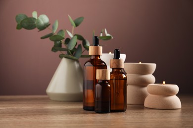 Photo of Spa composition with cosmetic products and burning candles on wooden table against brown background, closeup