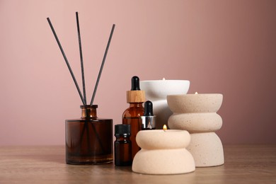 Photo of Spa composition with cosmetic products, burning candles and reed air freshener on wooden table against pink background, closeup