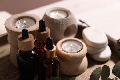 Photo of Cosmetic products and burning candles on tray against blurred background, closeup. Spa treatment