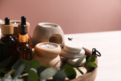 Photo of Cosmetic products, eucalyptus branch, spa stones and burning candles on tray against blurred background, closeup. Spa treatment