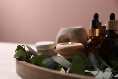 Photo of Cosmetic products, eucalyptus branch and burning candles on white wooden table against pink background, closeup. Spa treatment
