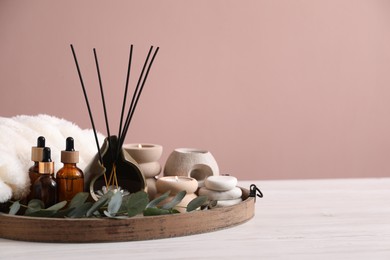 Photo of Spa composition of holder with incense sticks, burning candles and cosmetic products on white wooden table against pink background. Space for text