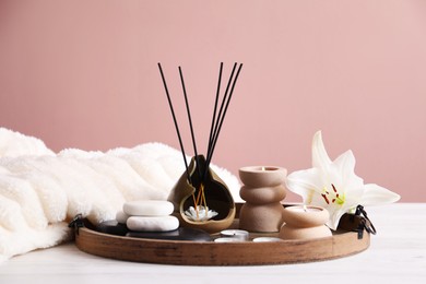 Photo of Spa composition of holder with incense sticks, burning candles and spa stones on white wooden table against pink background