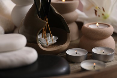 Photo of Holder with incense sticks, burning candles and spa stones on wooden tray, closeup