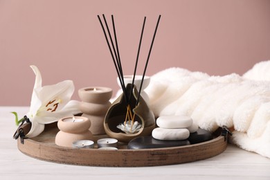 Photo of Composition with incense sticks, burning candles and spa stones on white wooden table against pink background, closeup