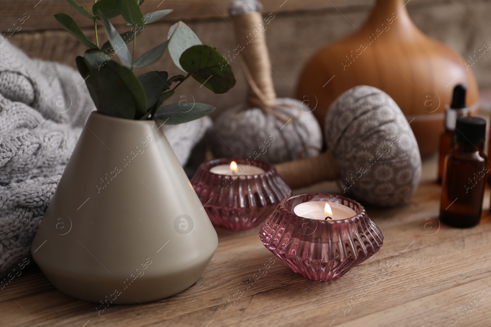 Spa composition with burning candles, vase with eucalyptus branches and herbal bags on wooden table, closeup Photo of Spa composition with burning candles, vase with eucalyptus branches and herbal bags on wooden table, closeup