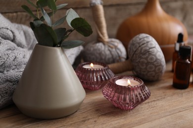 Photo of Spa composition with burning candles, vase with eucalyptus branches and herbal bags on wooden table, closeup