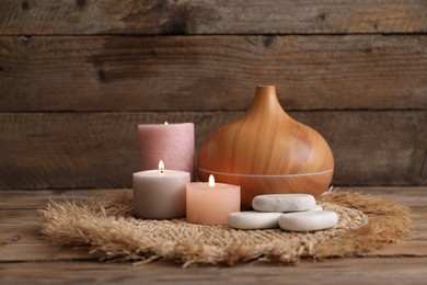 Photo of Composition with spa stones, aroma oil diffuser and burning candles on wooden table