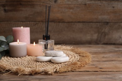 Photo of Composition with spa stones, reed air freshener and burning candles on wooden table, closeup. Space for text