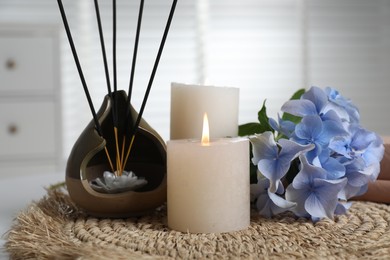 Photo of Spa composition of holder with incense sticks, burning candles and flowers on wicker mat indoors, closeup