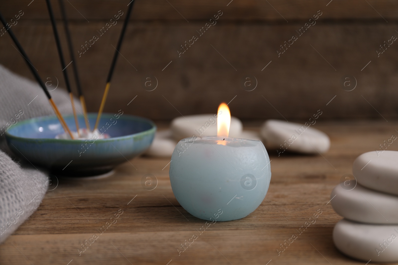 Burning candle, spa stones and incense sticks on wooden table, closeup Photo of Burning candle, spa stones and incense sticks on wooden table, closeup